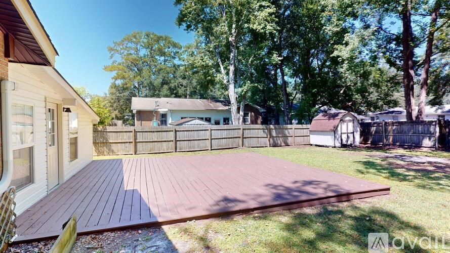 A wooden deck in a backyard with a house and trees in the background.