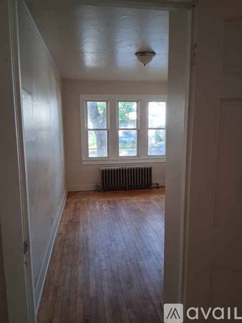 A room with wooden floors and a window with a view of trees and a radiator on the floor.