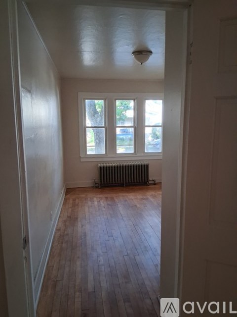 A room with wooden floors and a window with a view of trees and a radiator on the floor.