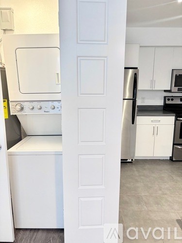A white door is open to a kitchen with a stove, refrigerator, and microwave.