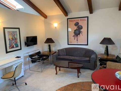 A living room with a grey couch, a red table, and a painting on the wall.
