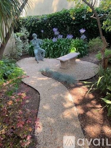 A small statue of a person is sitting on a bench in a garden.