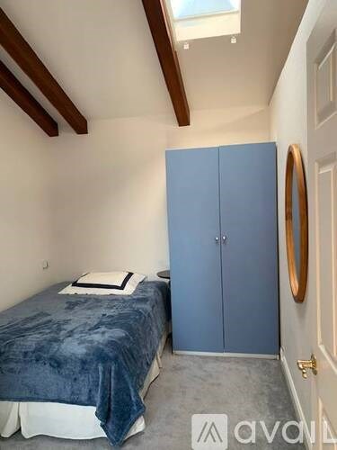 A bedroom with a bed, a blue wardrobe, and a round mirror on the wall.