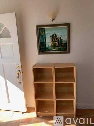 A painting hangs on a wall above a wooden shelf.