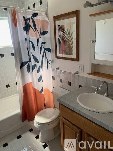 A bathroom with a white toilet, a sink, and a shower curtain with a leaf pattern.
