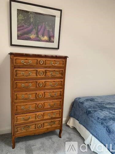 A wooden chest of drawers with a blue bed in the background.