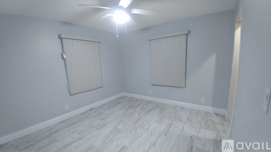 A room with a ceiling fan and light, and a wall with a window covered by blinds.
