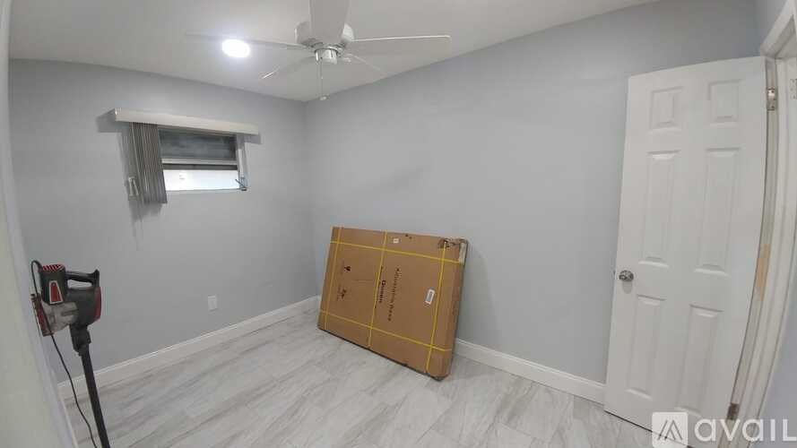 A room with a ceiling fan and a window with blinds, a box on the floor, and a door on the right.
