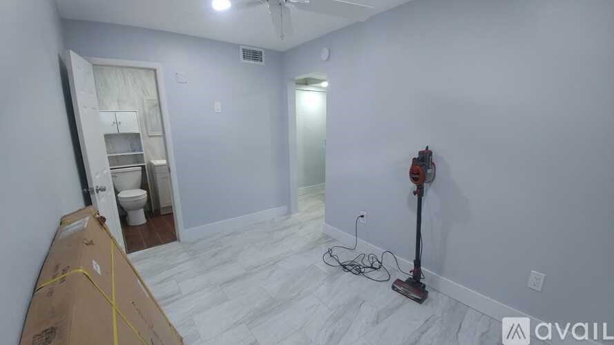 A room with a white floor and walls, a fan, and a vacuum cleaner.