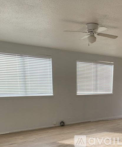 A room with a ceiling fan and two windows with blinds.