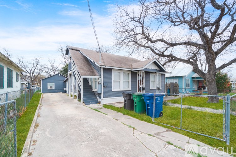 A blue house with a grey roof and a green trash bin in front.