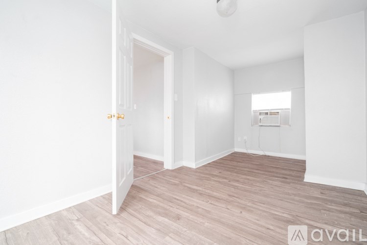 A room with a wooden floor and white walls, with a door open to another room.