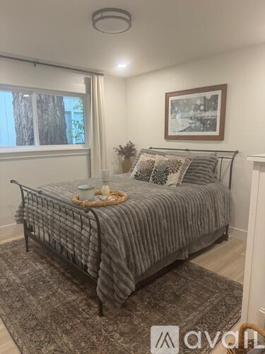 A bedroom with a bed, pillows, a blanket, a vase with flowers, a picture on the wall, and a window with blinds.