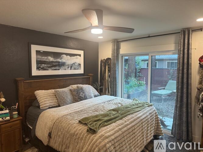 A bedroom with a bed, a ceiling fan, and a window with a view of the backyard.
