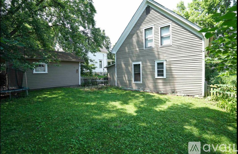 A house with a brown siding and a white roof is surrounded by a green lawn.