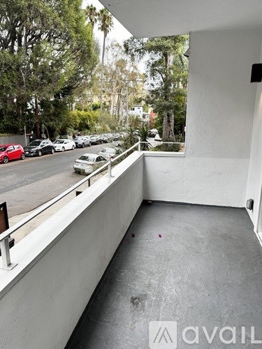A balcony with a white wall and a black railing overlooks a parking lot.