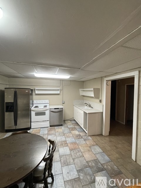 A kitchen with a table and chairs in the foreground and a refrigerator, oven, and sink in the background.