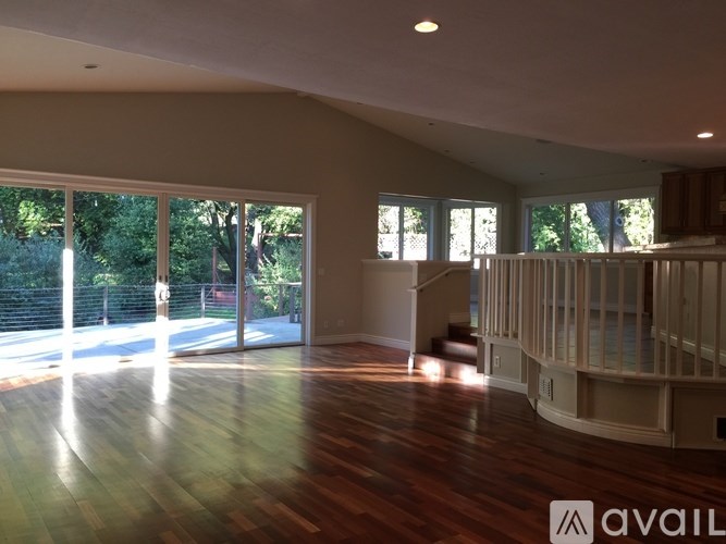 A spacious room with wooden floors and large windows overlooking a backyard.