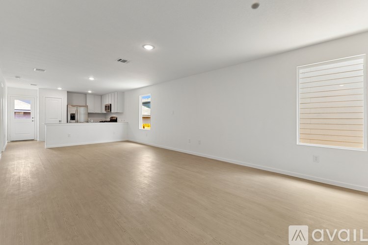 A spacious room with wooden flooring and a window with blinds.