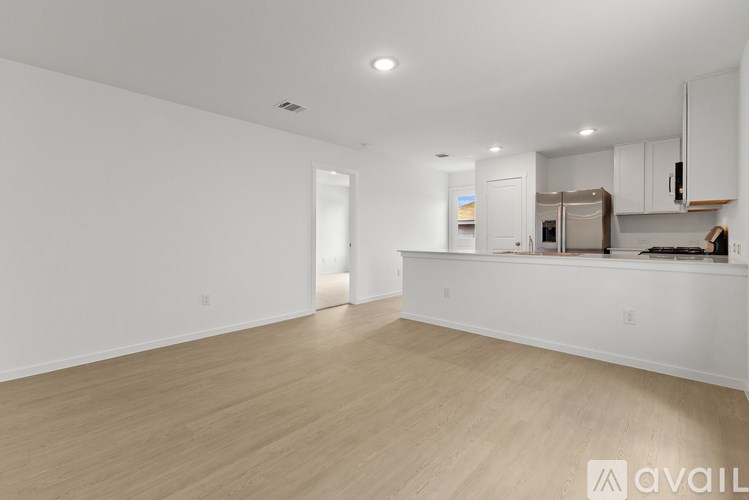 A spacious kitchen and living room with white walls and wooden flooring.