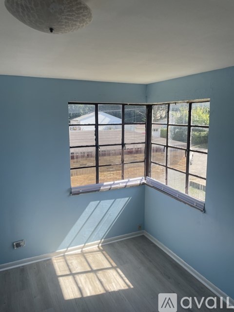 A room with a large window and a view of a fence and trees outside.