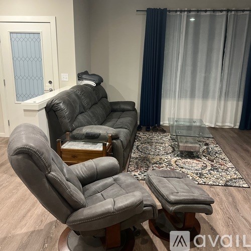 A grey leather sofa and chair set in a room with a glass table and a rug.
