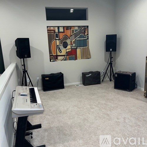 A room with a piano, speakers and a painting of a guitar on the wall.