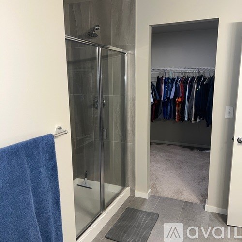 A bathroom with a walk-in shower and a closet with clothes hanging.