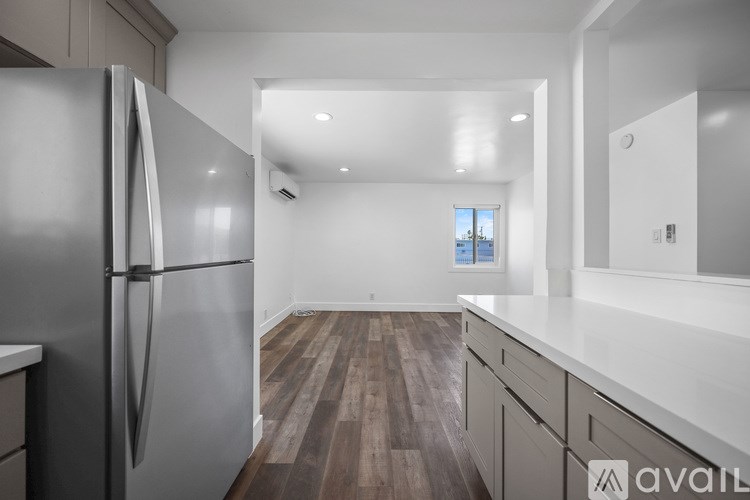 A kitchen with a refrigerator, wooden floors, and white walls.