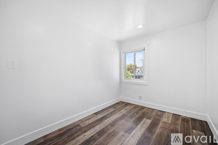 A room with wooden flooring and a window showing a view of trees and buildings outside.