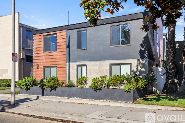A modern two-story building with a grey and brown facade and green plants in front.