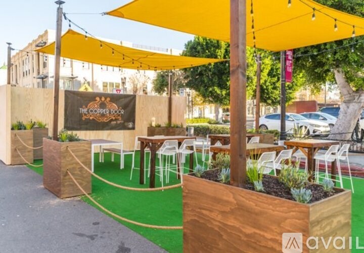 A patio area with wooden planters and white chairs under yellow umbrellas.