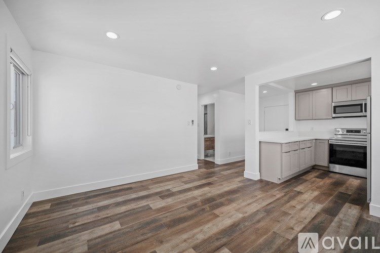 A spacious kitchen with wooden flooring and white walls.