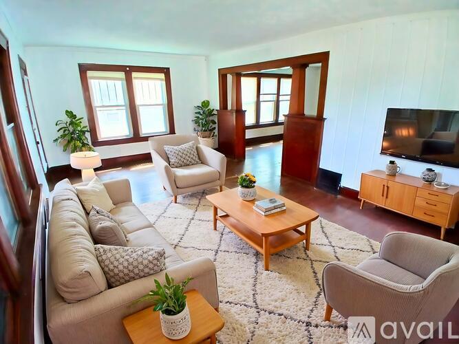 A living room with a white couch, a grey armchair, a wooden coffee table, and a television.