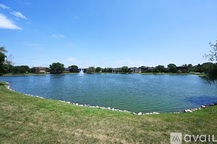 A large body of water surrounded by grass and buildings in the distance.