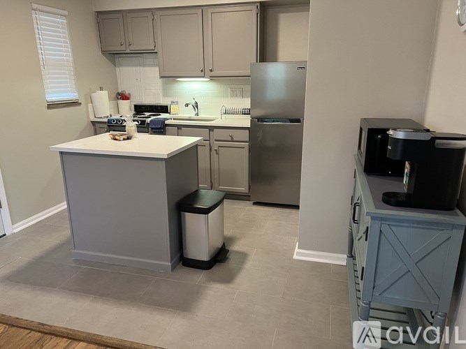 A kitchen with a stove, refrigerator, and trash can.
