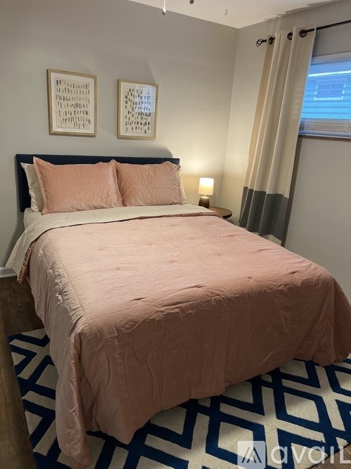 A bed with a pink cover and two pink pillows in a room with a blue and white patterned carpet.