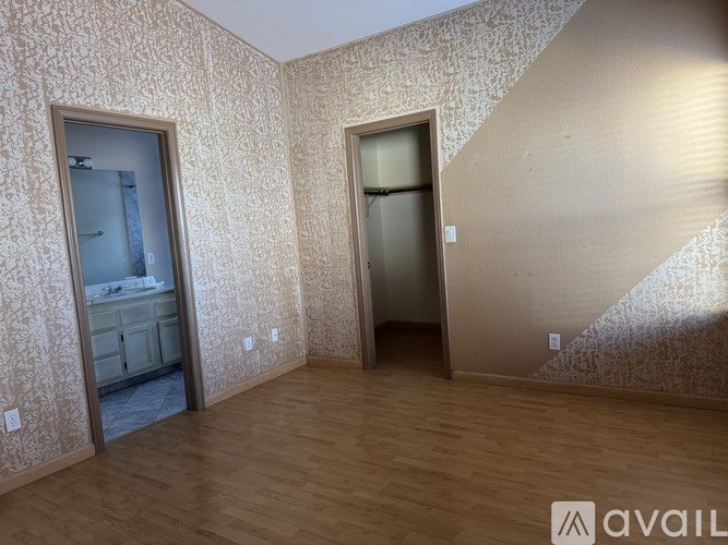 A room with wooden floors and patterned wallpaper with two doors.