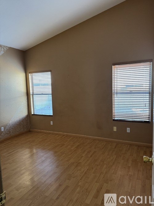 A room with wooden flooring and two windows with blinds.