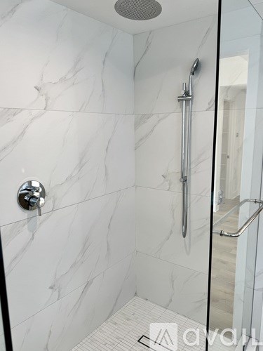 A white marble tiled shower with a glass door.