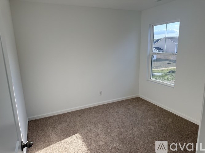 A room with a carpeted floor and a window showing a view of a house.