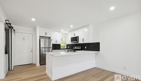 A modern kitchen with white cabinets and a wooden floor.