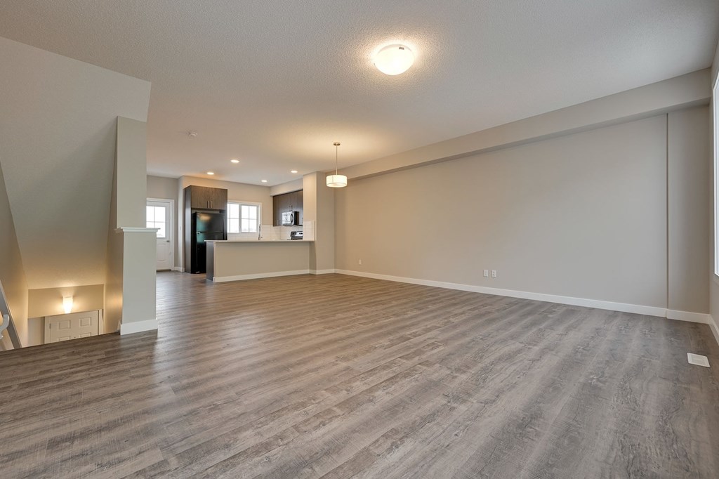 A spacious room with wooden flooring and a fireplace on the left side.