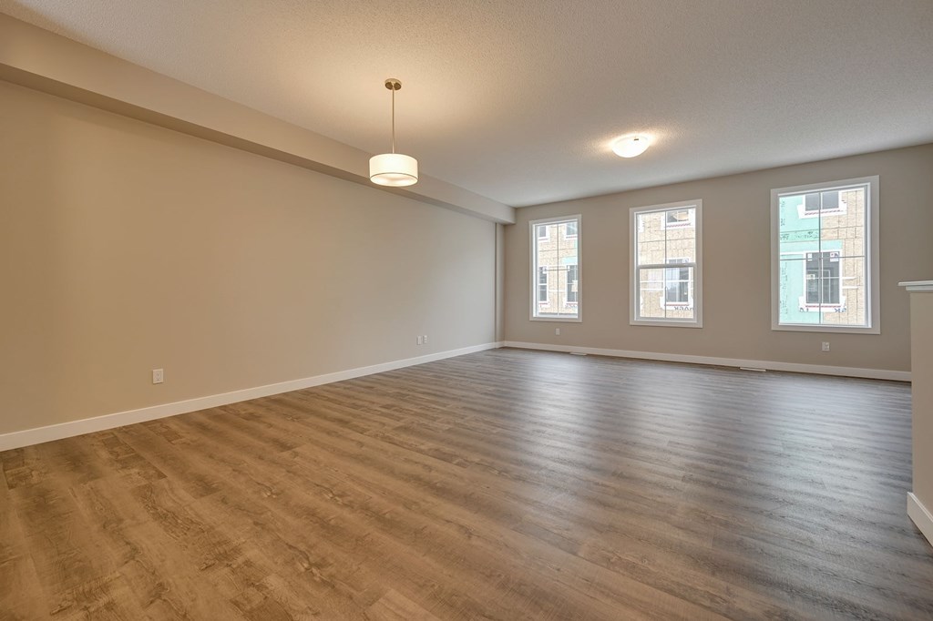 Empty room with wooden flooring and three windows.