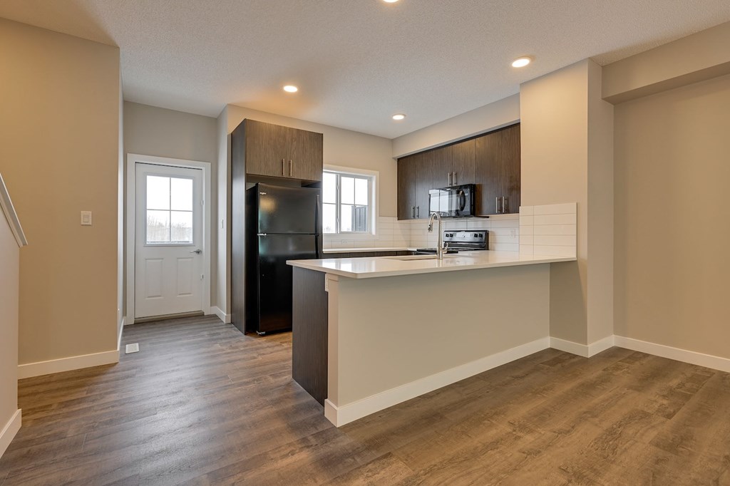 A kitchen with a black refrigerator and wooden floors.