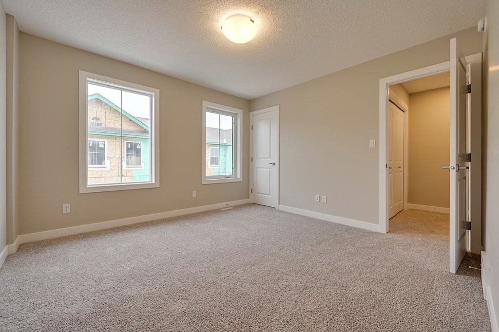 A spacious room with carpeted floor and two windows.