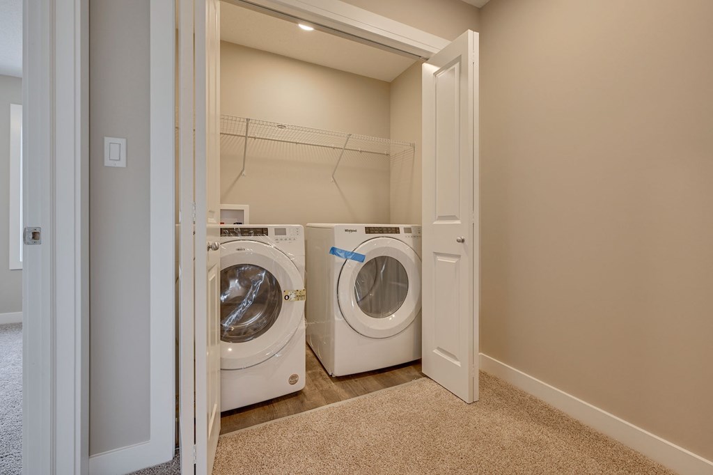A laundry room with two washing machines and a carpeted floor.
