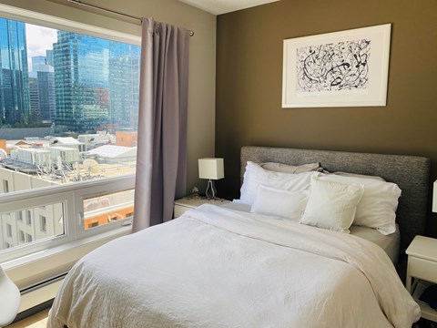 A bedroom with a large bed and a city view through the window.