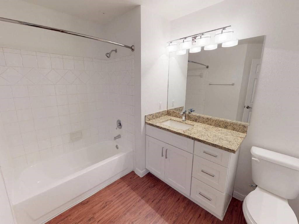 A white bathroom with a marble counter top and wooden floors.
