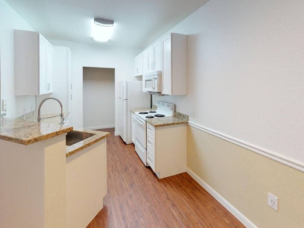 A kitchen with wooden floors and white cabinets.